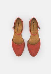 Zapatos planos de mujer de cuero rojo con correas al tobillo y hebillas, plantillas de color marrón etiquetadas "El Naturalista", vistos desde arriba sobre un fondo blanco.