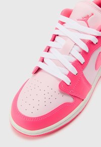 Gros plan d'une basket rose et blanche avec des lacets blancs, un bout perforé et un logo Jumpman cousu sur la languette.