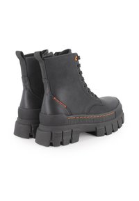 Botas de tobillo negras hechas de material sintético, con una suela gruesa, acentos de costura en naranja y ojales de metal para los cordones.