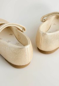 Goldene Ballerinas mit strukturierter Oberfläche, flacher Sohle und einem dünnen Riemen über dem Spann. Innenraum mit hellem Muster gefüttert.