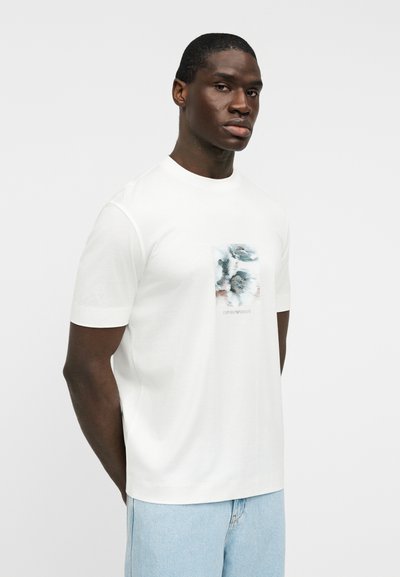 Άσπρο κοντομάνικο μπλουζάκι από απαλό ύφασμα, με τυπωμένο σχέδιο στο μπροστινό μέρος με μπλε και γκρι αποχρώσεις, στρογγυλή λαιμόκοψη.