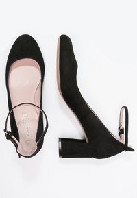 Schwarze Wildleder-High-Heels mit quadratischer Zehenpartie, Knöchelriemen und blockiertem Absatz. Weiche Innenauskleidung in Hellrosa. Glatte Textur.