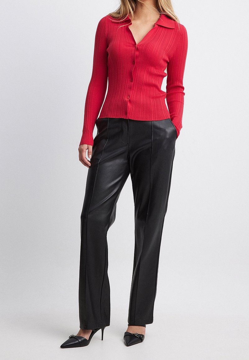 Chemise rouge côtelée à manches longues avec boutons, associée à un pantalon en cuir noir taille haute, le tout complété par des talons noirs pointus.