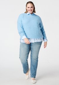 Lichtblauwe, pluizige trui over een wit overhemd met blauwe strepen, gecombineerd met lichtblauwe spijkerbroek en witte schoenen met polka dots.