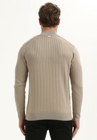 Jersey de punto acanalado beige con mangas largas y cuello redondo. Detalles de costura sutiles a lo largo de los hombros y la espalda, textura suave.