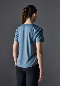 Light blue short-sleeve athletic shirt with a smooth texture, paired with black leggings; viewed from the back, showing braided hair.
