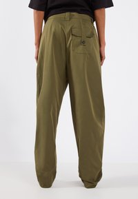 Pantalons à jambes larges vert olive avec une poche arrière, fabriqués en tissu lisse, dotés d'une fermeture à bouton et de poignets fuselés.
