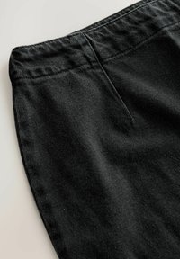 Black corduroy pants with a textured surface, featuring a smooth waistband and a flat front pocket. Close-up view highlighting fabric details.
