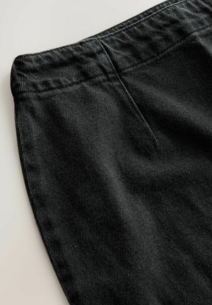 Pantaloni din corduroy negri cu o textură distinctă, având un tiv neted și un buzunar frontal plat. Vedere de aproape care evidențiază detaliile materialului.