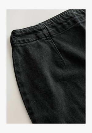 Black corduroy pants with a textured surface, featuring a smooth waistband and a flat front pocket. Close-up view highlighting fabric details.