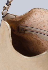 Beżowa torebka skórzana z gładką podszewką, z wewnętrzną kieszonką na zamek oraz powracającym wzorem logo na jasnym tle.