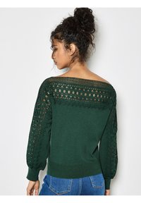 Suéter verde con intrincados detalles de encaje en los hombros y las mangas, puños acanalados y una textura suave. Diseñado con un ajuste holgado.