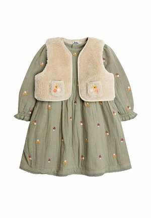 Grünes langärmliges Kleid mit kleinen Blumen- und Pilzstickereien, kombiniert mit einer cremefarbenen, kuscheligen Weste mit aufgesetzten Taschen.