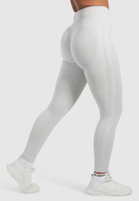 Hochgeschnittene weiße Leggings mit einem gerippten Bund und vertikalen Nahtdetails, kombiniert mit hellen Sneakers. Glattes, elastisches Material.