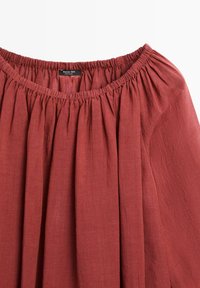 Rust-red off-shoulder top with elastic neckline and gathered fabric, featuring a Massimo Dutti label inside the collar.