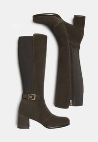 Brune ruskind nederdele støvler med blokhæle, lynlås i siden, elastisk bagpanel og dekorativt guldbuckle på ydersiden af anklen.