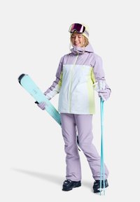 Strój narciarski składa się z fioletowo-białej kurtki z żółtymi akcentami, dopasowanych fioletowych spodni oraz miętowego kija narciarskiego i deski snowboardowej.