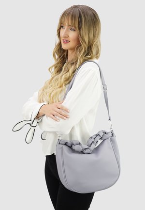 Grijze leren schoudertas met een gevlochten handvat, gladde textuur, afgeronde vorm en verstelbare band, afgebeeld tegen een effen achtergrond.