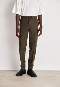 Olivgröna byxor med elastisk midja och dragsko, tapered design och sidofickor, kombinerade med svarta ankelstövlar.