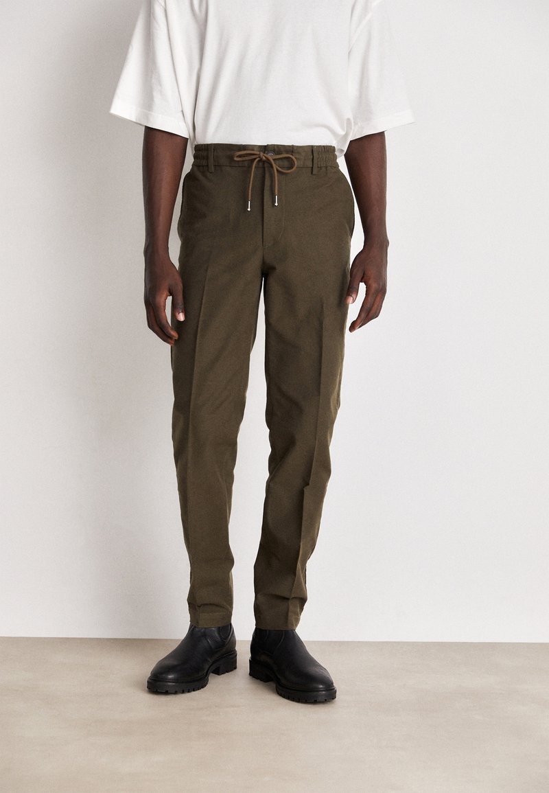 Olivgröna byxor med elastisk midja och dragsko, tapered design och sidofickor, kombinerade med svarta ankelstövlar.