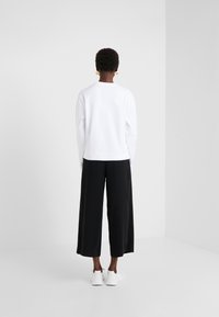 Felpa bianca con maniche lunghe e scollatura rotonda abbinata a pantaloni neri a gamba larga e sneakers bianche; tessuto morbido e design classico.