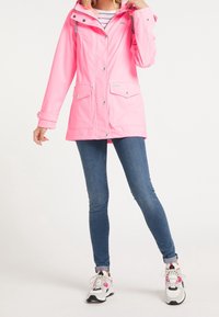 Rosa vattentät parkas med huva, tryckknappar och två framfickor. Bärs över blå jeans och vita sneakers med rosa detaljer.