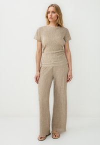 Lichtbeige gebreide top en wijde broek, met verticale strepen. Zachte textuur, korte mouwen en een relaxte pasvorm. Gemaakt met eenvoudige sandalen.