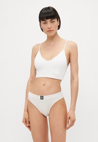 Bralette en coton blanc avec des fines bretelles et un décolleté en V profond, associé à un slip blanc assorti avec une ceinture de logo noire.