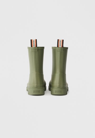 Botas de chuva verdes de borracha com uma textura suave, altura até à meia-caneleira, e alças de puxar laranja e preta em contraste na parte de trás.