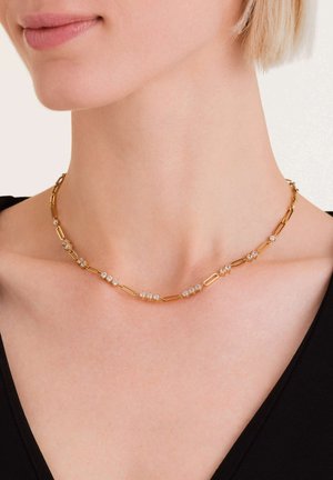 Gouden metalen ketting met langwerpige schakels en kleine, heldere decoratieve stenen die gelijkmatig zijn verdeeld. Ontworpen om op de sleutelbeen te liggen.