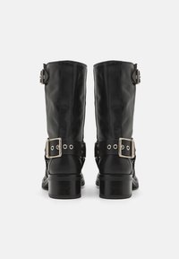 Botas de cuero negro con una altura a media pantorrilla, tacón cuadrado, hebillas laterales y acentos de herrajes plateados. Cuero texturizado con costuras visibles.