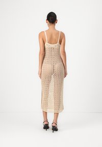 Knee-length, beige crochet dress with thin straps and open weave design, featuring side slits for ease of movement.
