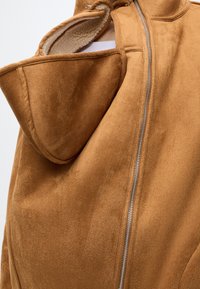 Veste en daim marron avec fermeture éclair métallique apparente et doublure polaire douce à l'intérieur de la capuche attachée.