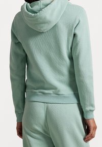 Mintgrön hoodie med dragsko, ribbade ärmar och fållar, tillverkad av mjukt material, i kombination med matchande joggers.