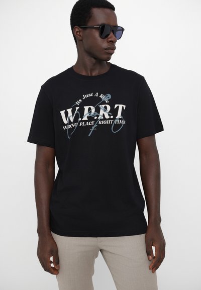 Tricou negru din bumbac cu text grafic alb și albastru „W.P.R.T. WRONG PLACE RIGHT TIME.” Mâneci scurte și croială lejeră.
