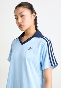 Svijetloplava sportska košulja s tamnoplavim ovratnikom, s vertikalnim prugama, kratkim rukavima i Adidas logom na prsima.