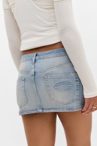 Kvinna iklädd en ljusblå denimminij skirt med bakfickor, en av dem märkt "BDG," i kombination med en åtsittande vit långärmad topp.
