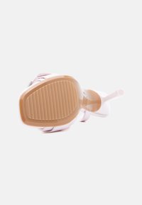 Μονό ανοιχτό ροζ πέδιλο με ψηλό τακούνι, εμφανιζόμενο από κάτω με τραχιά καφετιά σόλα και λεπτό τακούνι πάνω σε λευκό φόντο.