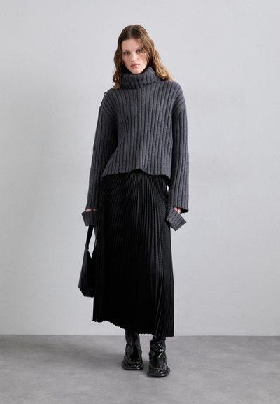 Suéter cinza com gola alta e textura canelada, com a bainha sem acabamento, combinado com uma saia maxi plissada preta e botas brilhantes até ao joelho. Bolsa preta simples.