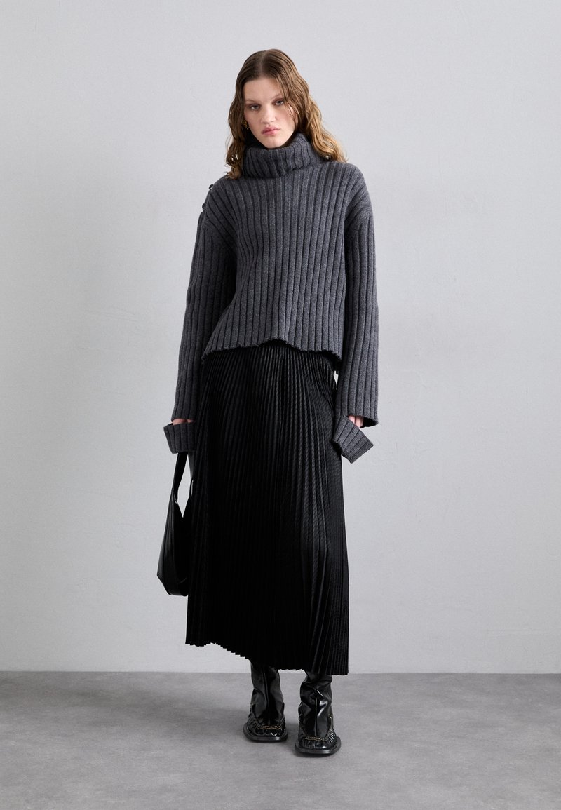 Grijze geribbelde coltrui met een rauwe zoom, gecombineerd met een zwarte geplooide maxi rok en glanzende kniehoge laarzen. Eenvoudige zwarte handtas.