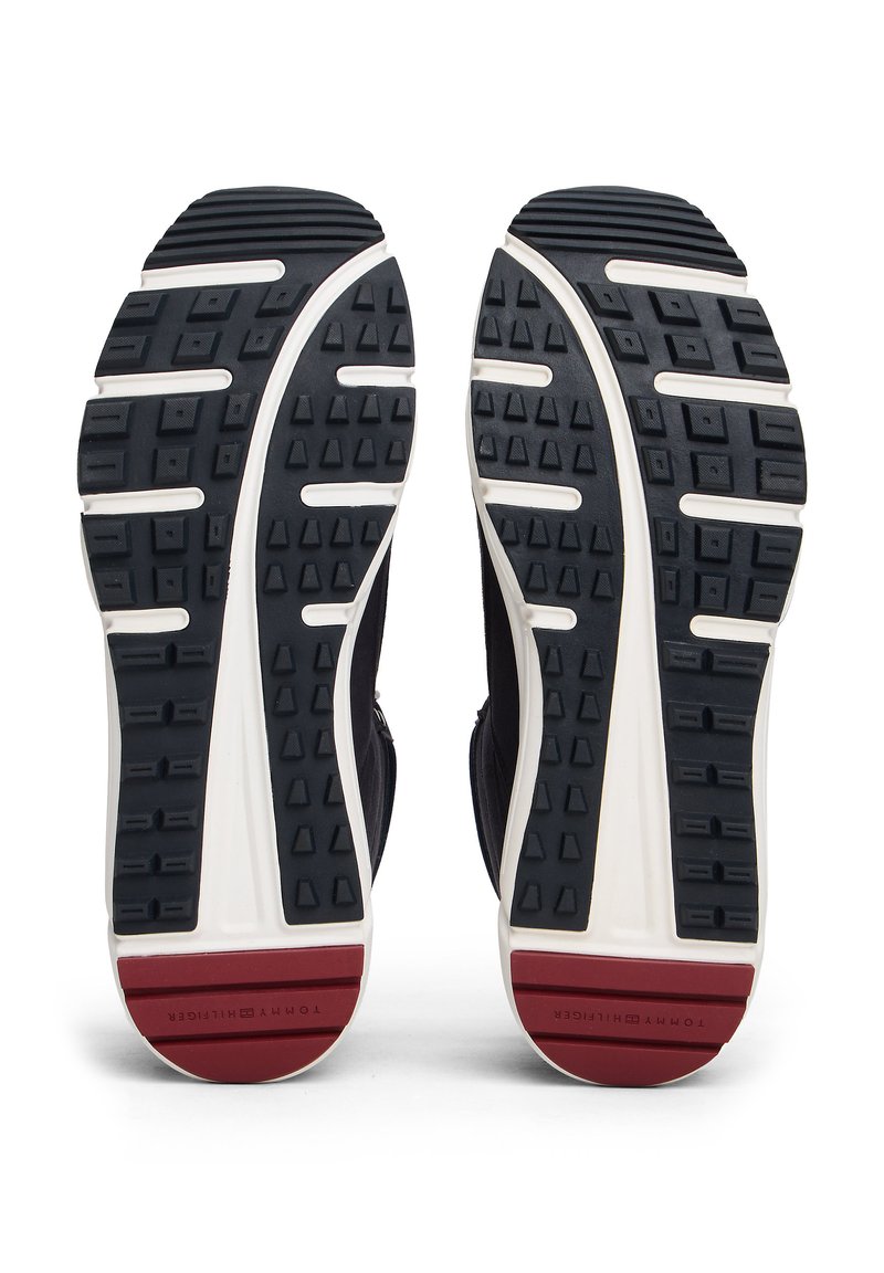 Black athletic shoes with textured rubber outsoles featuring triangular lugs and white midsole. Red accents near the heel with branding.
