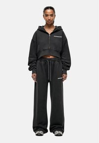 Felpa nera cropped con zip frontale e maniche ampie, abbinata a pantaloni della tuta neri larghi con vita elastica e dettaglio del logo.