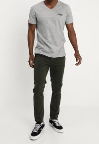 Camiseta gris de cuello en V, pantalones verdes de corte ajustado y zapatillas negras con detalles en blanco y suela texturizada.