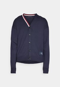 Navyblauer Cardigan mit V-Ausschnitt, weißen und roten gestreiften Kragen, sieben schwarzen Knöpfen und gerippten Bündchen. Verfügt über ein kleines Logo-Patch am Saum.
