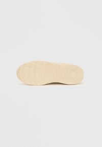 Kremfarget sneakersåle med et teksturert gummimønster, med dype spor og sirkulære detaljer for godt grep. Flat og avrundet design.