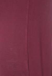 Bordová pletená látka s hladkou texturou, s jemným leskem a vertikálním švem na jedné straně.