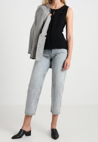 Top negro sin mangas con pliegues, blazer gris claro, jeans de pierna ancha azul claro y mocasines negros de tacón cuadrado. Atuendo simple y casual.