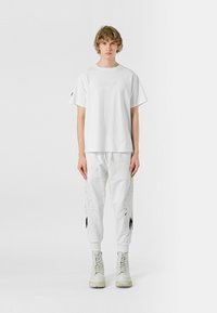 Camiseta blanca oversized y pantalones de chándal a juego con diseños bordados. Tejido texturizado. Botas blancas con cordones y suelas planas.