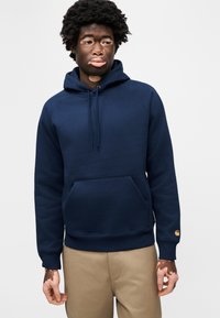 Μπλε ναυτικό φούτερ με κουκούλα από βαμβακερό μείγμα· διαθέτει μπροστινή τσέπη καγκουρό, ριμπ μανσετές και ένα μικρό λογότυπο στο μανίκι.