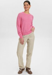 Rožinė megzta megztinis su apvalia iškirpte, derinamas su smėlio spalvos tekstūruotomis kelnėmis ir rudais šnarelių batais. Paprastas, kasdieniškas aprangos derinys.